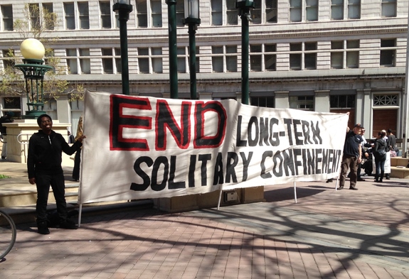 A banner is held at Oscar Grant Plaza as part of the Statewide Coordinated Actions to End Solitary Confinement on March 23. (San Fransisco Bay View)