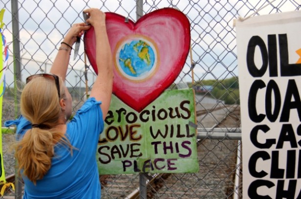 A protester with the Break Free action in Albany tapes a piece of art that reads, “ferocious love will save this planet,” to a fence blocking entry to the Port of Albany. (WNV / William Fowler)
