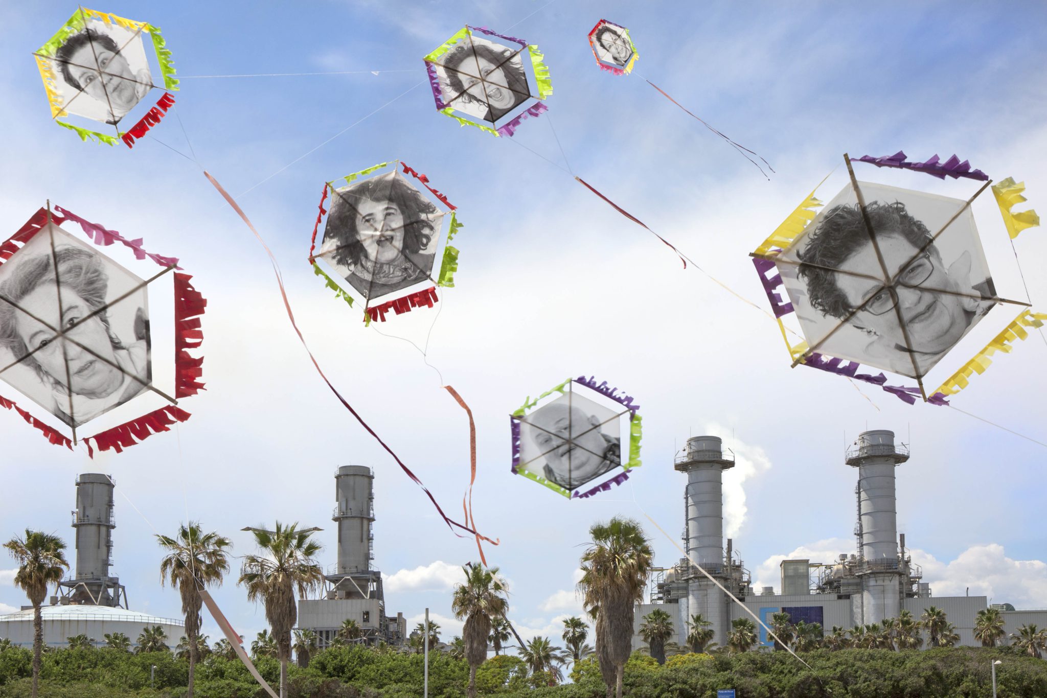 Large kites with people's faces fly over a power plant