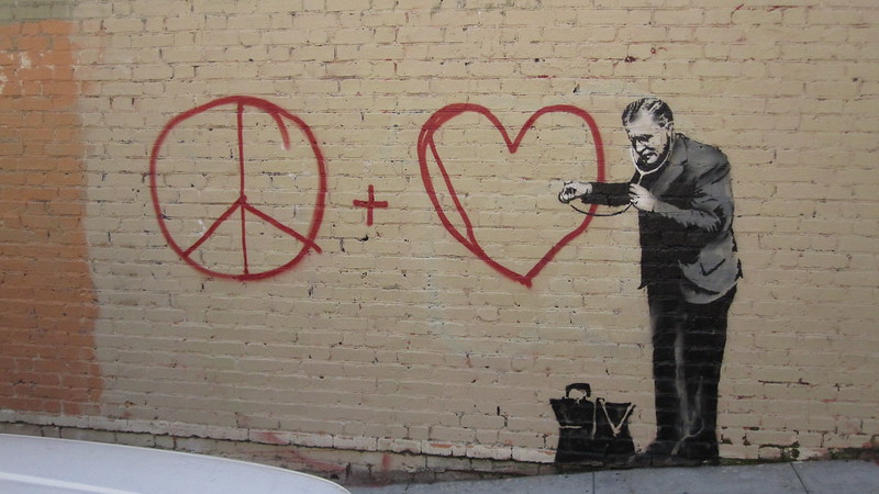 street art by banksy of a doctor checking for a pulse on a heart