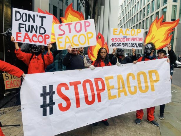 Activists hold signs in London's financial district to protest the insurance companies behind EACOP