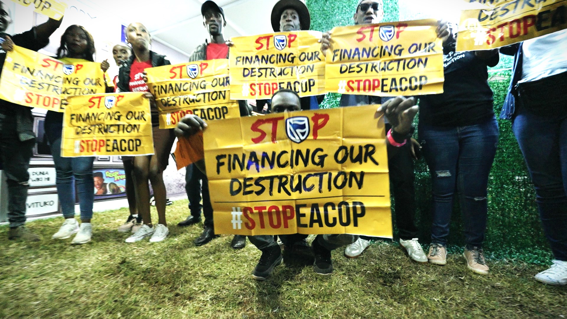 Protesters hold signs calling to stop the financing of EACOP